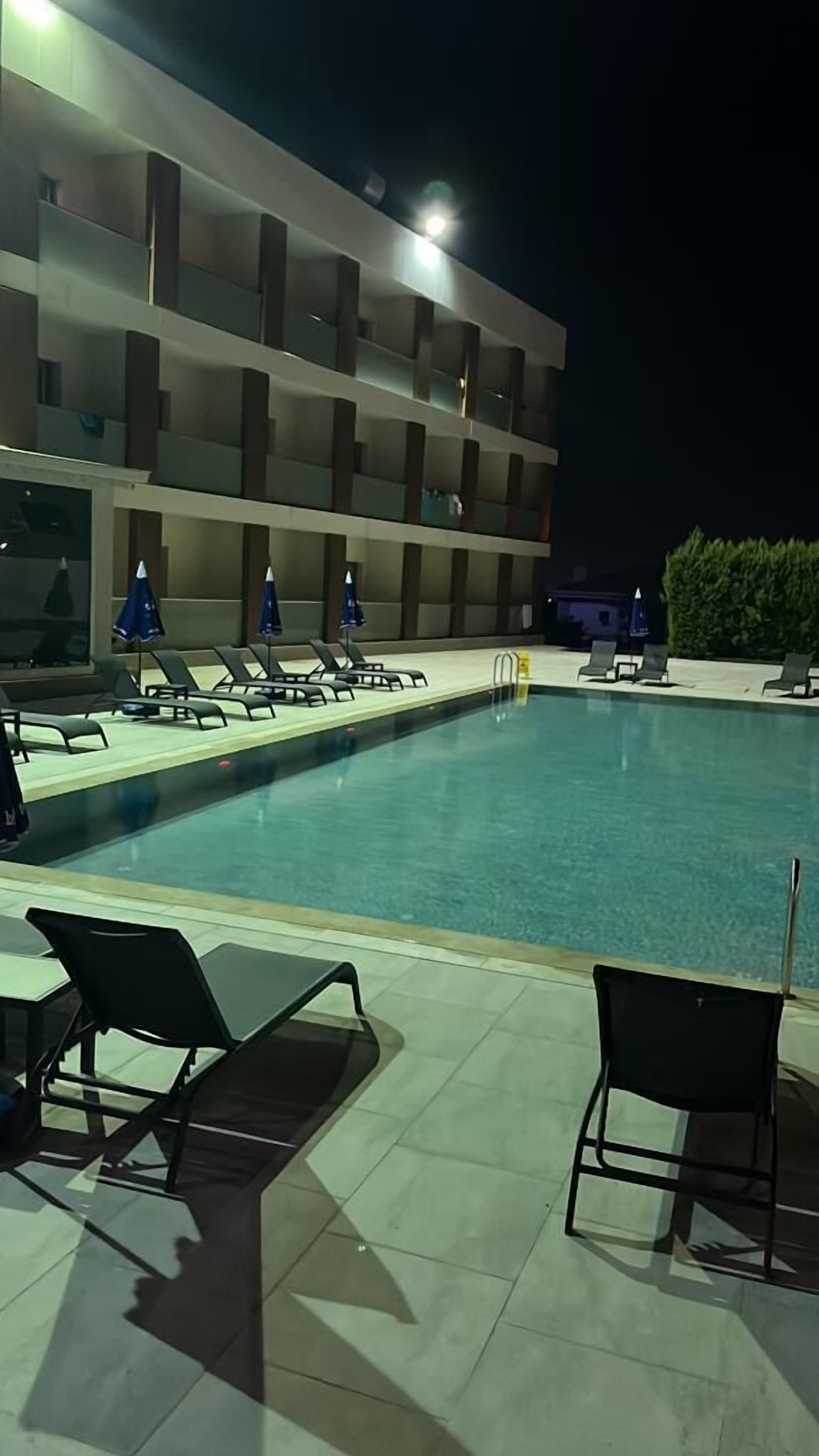 Una piscina con sillas de descanso y sombrillas, rodeada por un edificio con varios balcones.