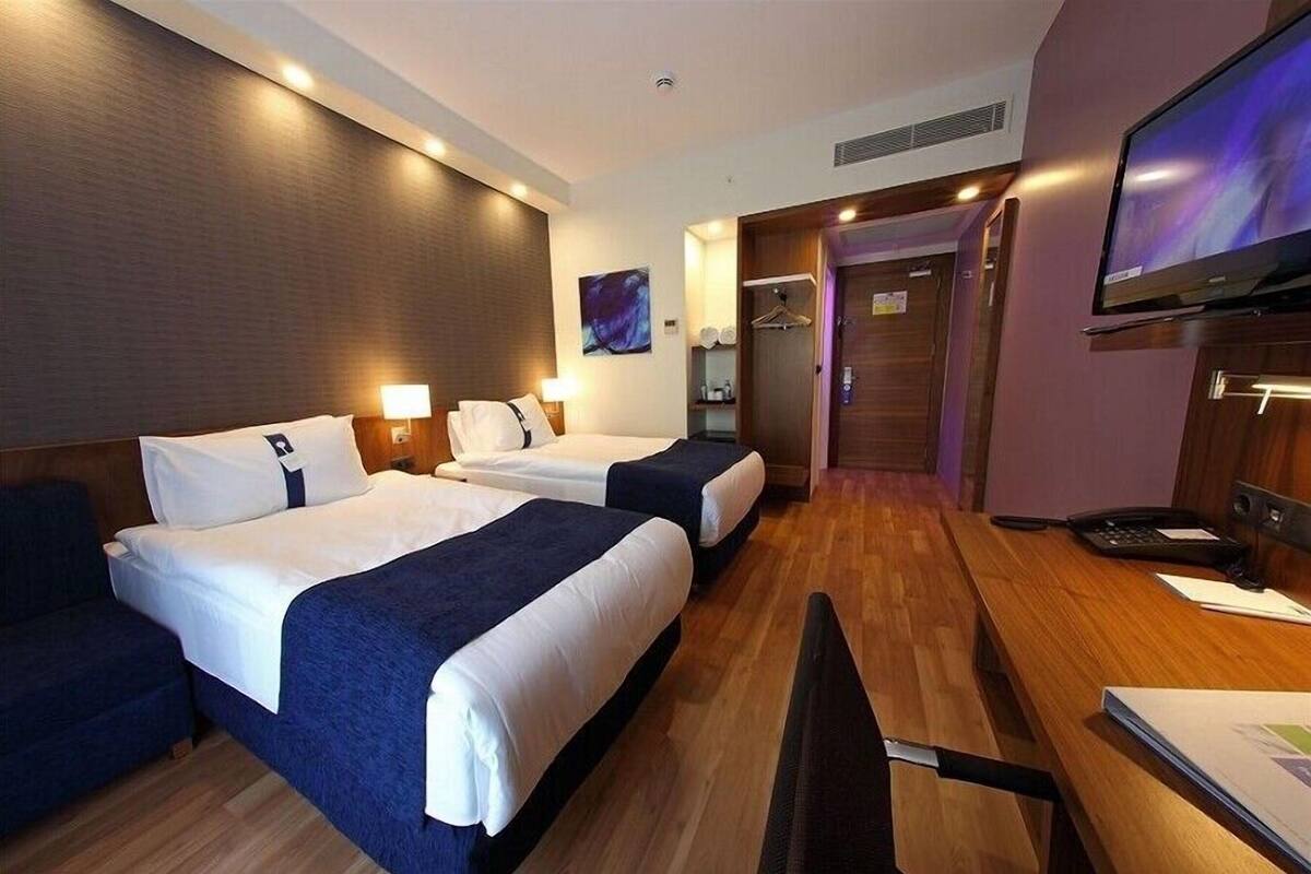 A hotel room with two beds, a desk, a TV, and a wooden floor.