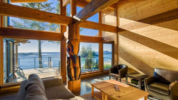 A spacious living area with a large window overlooking a scenic view, wooden beams, and a modern fireplace. - Wya Point Resort (Ucluelet)