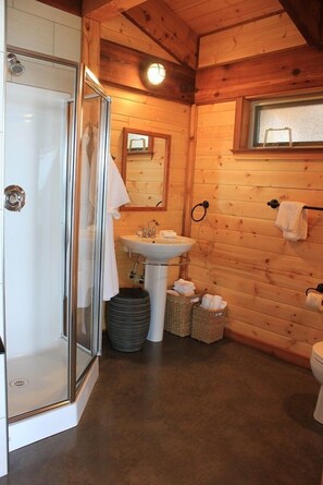 A wooden cabin bathroom with a glass shower enclosure, a sink, and a toilet. - Wya Point Resort (Ucluelet)