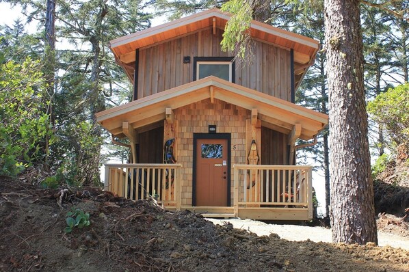 A two-story wooden cabin with a balcony, surrounded by trees. - Wya Point Resort (Ucluelet)
