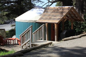 Una cabaña rústica con un porche cubierto, una pequeña construcción de madera y mobiliario exterior.