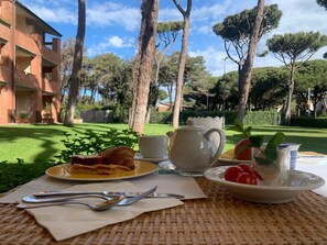 Une table dressée à l’extérieur, avec un croissant, une théière, une tasse et une assiette de tomates cerises.