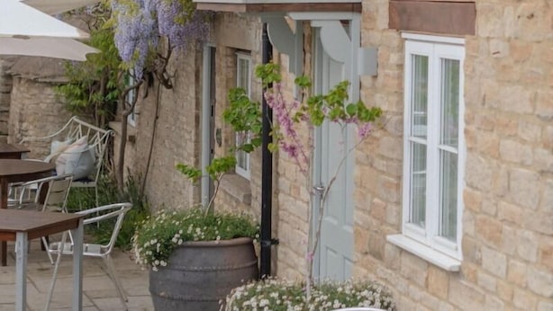 A stone building with a patio area featuring outdoor seating and potted plants. - The Bell at Hampton Poyle (Kidlington)