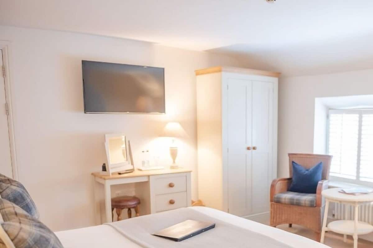 A bedroom with a bed, bedside table, lamp, wardrobe, chair, and a TV mounted on the wall.