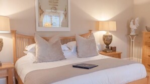 A neatly made bed with white linens and two pillows, a bedside table with a lamp, and a framed picture on the wall. - The Bell at Hampton Poyle (Kidlington)