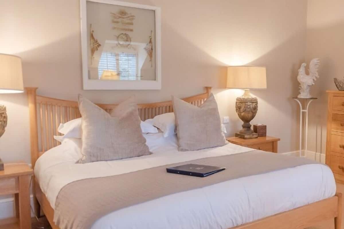 A neatly made bed with white linens and two pillows, a bedside table with a lamp, and a framed picture on the wall.