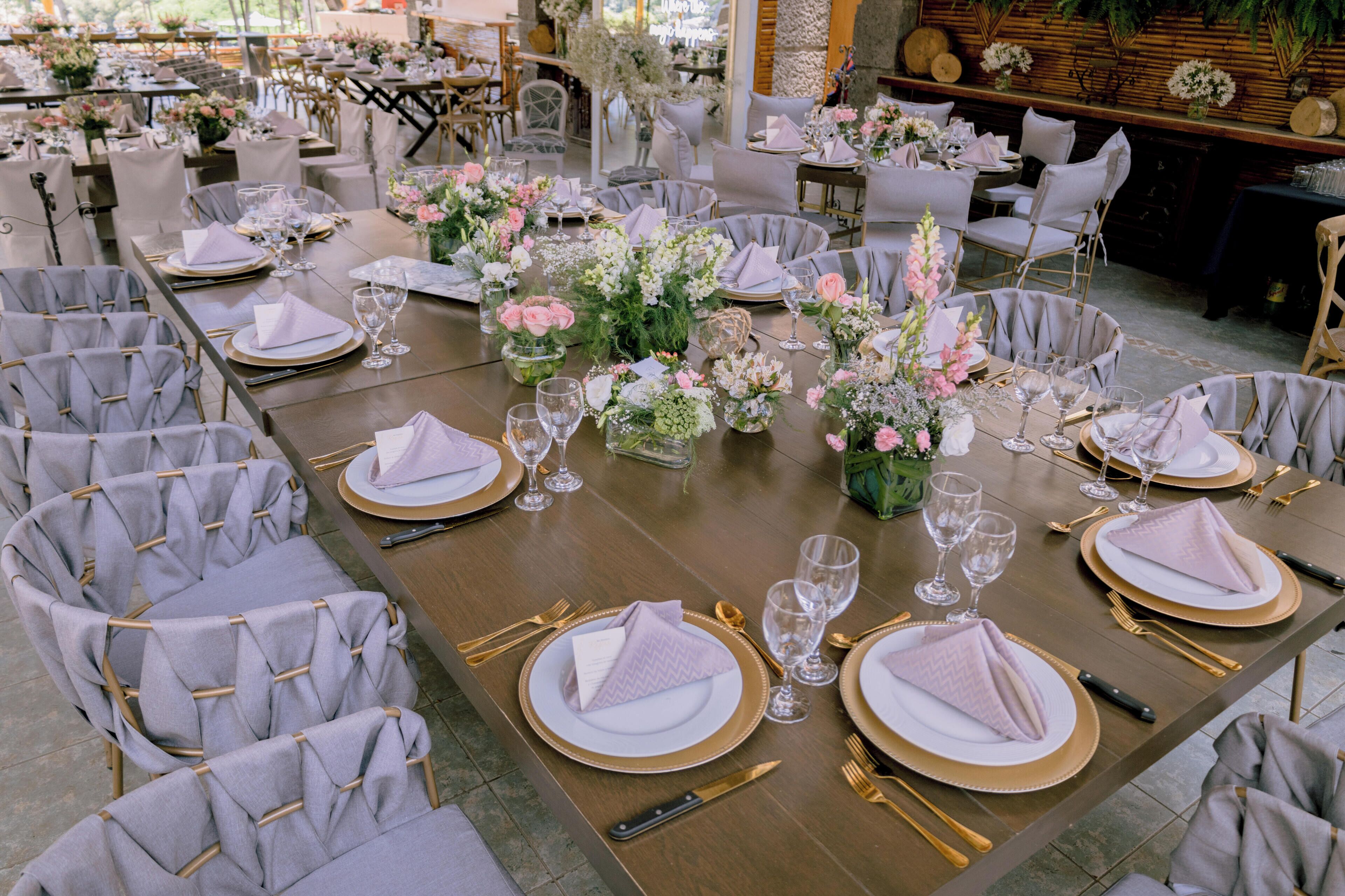 Une salle de banquet avec des tables rondes dressées pour un événement formel, agrémentée de compositions florales et de vaisselle bordée d’or.