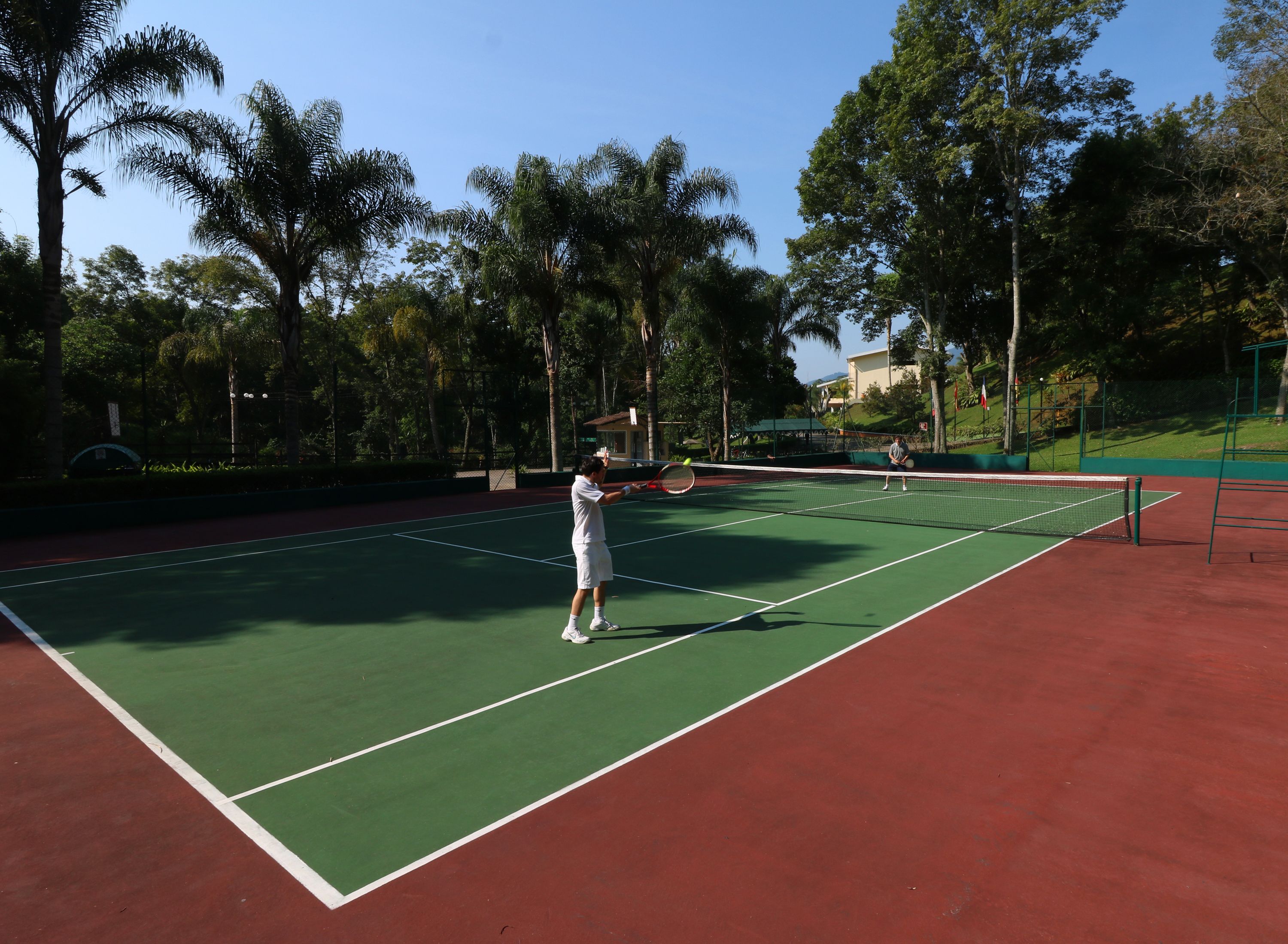 A tennis court with a net, surrounded by trees and a building in the background.