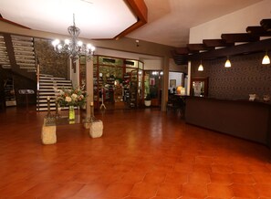 Un vestíbulo amplio con piso de madera, un mostrador de recepción, una araña y una escalera que conduce a los pisos superiores.
