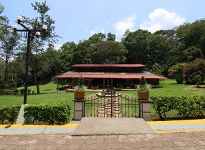 Un edificio con techo rojo y una zona de acceso pavimentada con una reja.