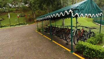 Ein überdachter Fahrradparkplatz mit einer Reihe Fahrräder, einem befestigten Weg und Grünflächen im Hintergrund.