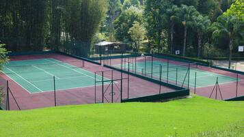 A tennis court with a net, surrounded by trees and a small building.
