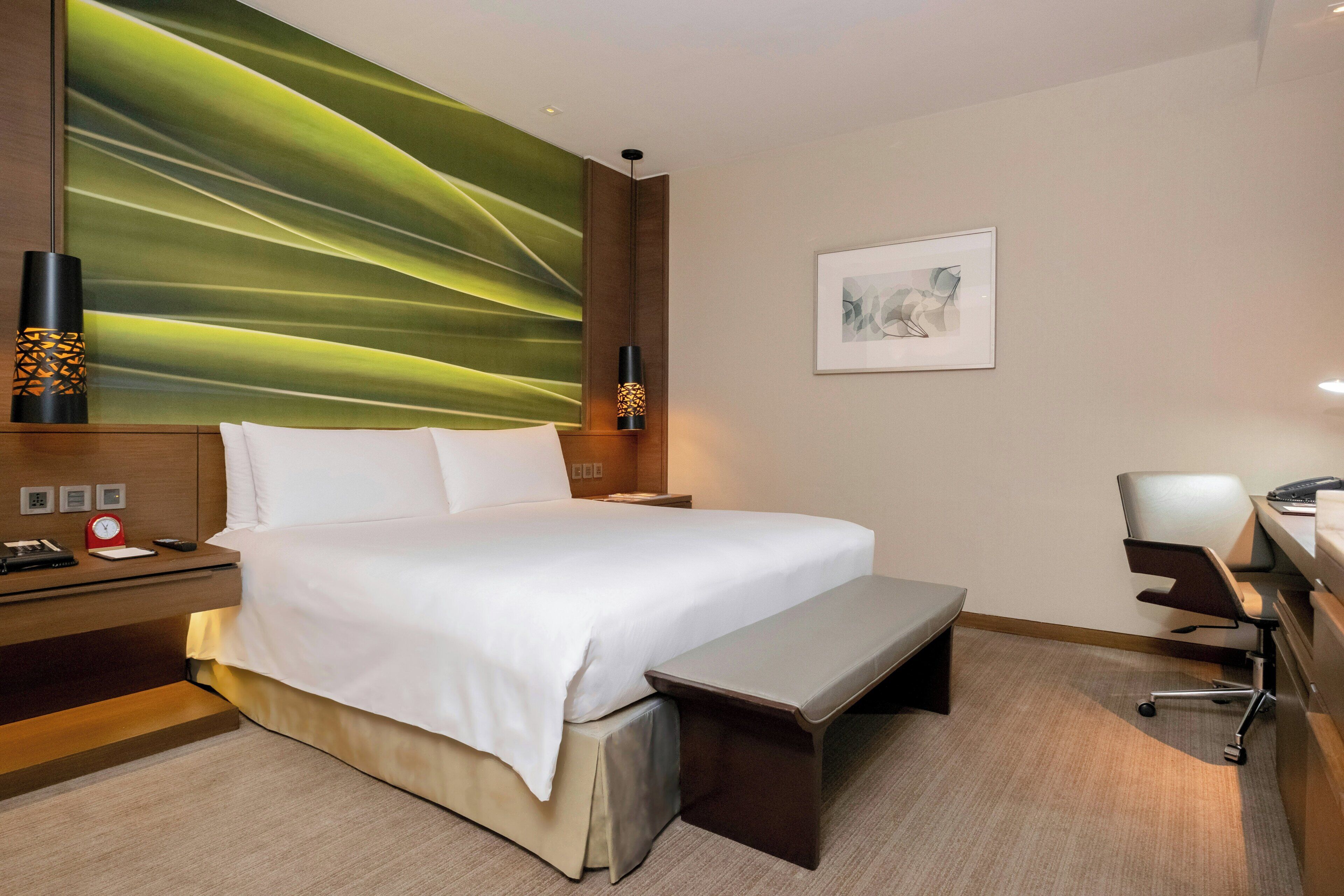 Une chambre d’hôtel avec un grand lit, des tables de chevet, un bureau avec une chaise, une lampe fixée au mur et un tableau.