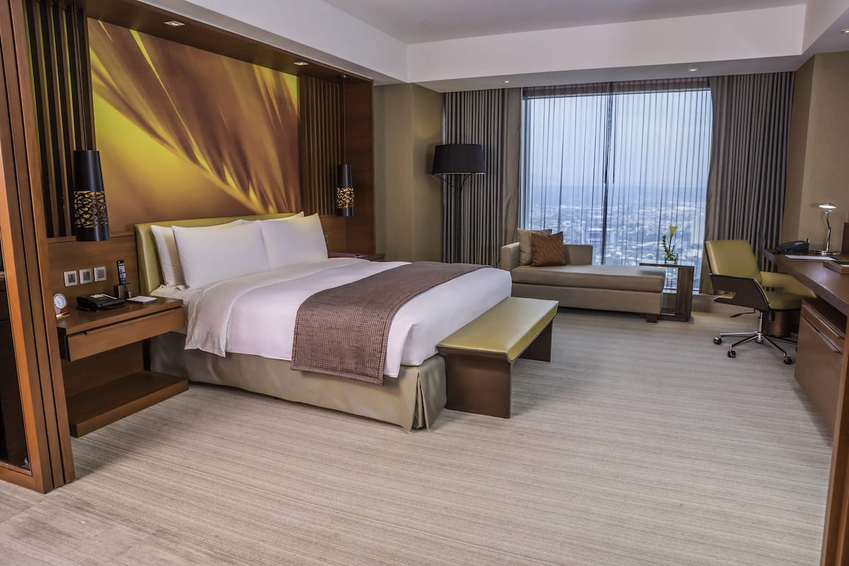 A modern hotel room with a large bed, a sofa, a desk, and a view of the city.