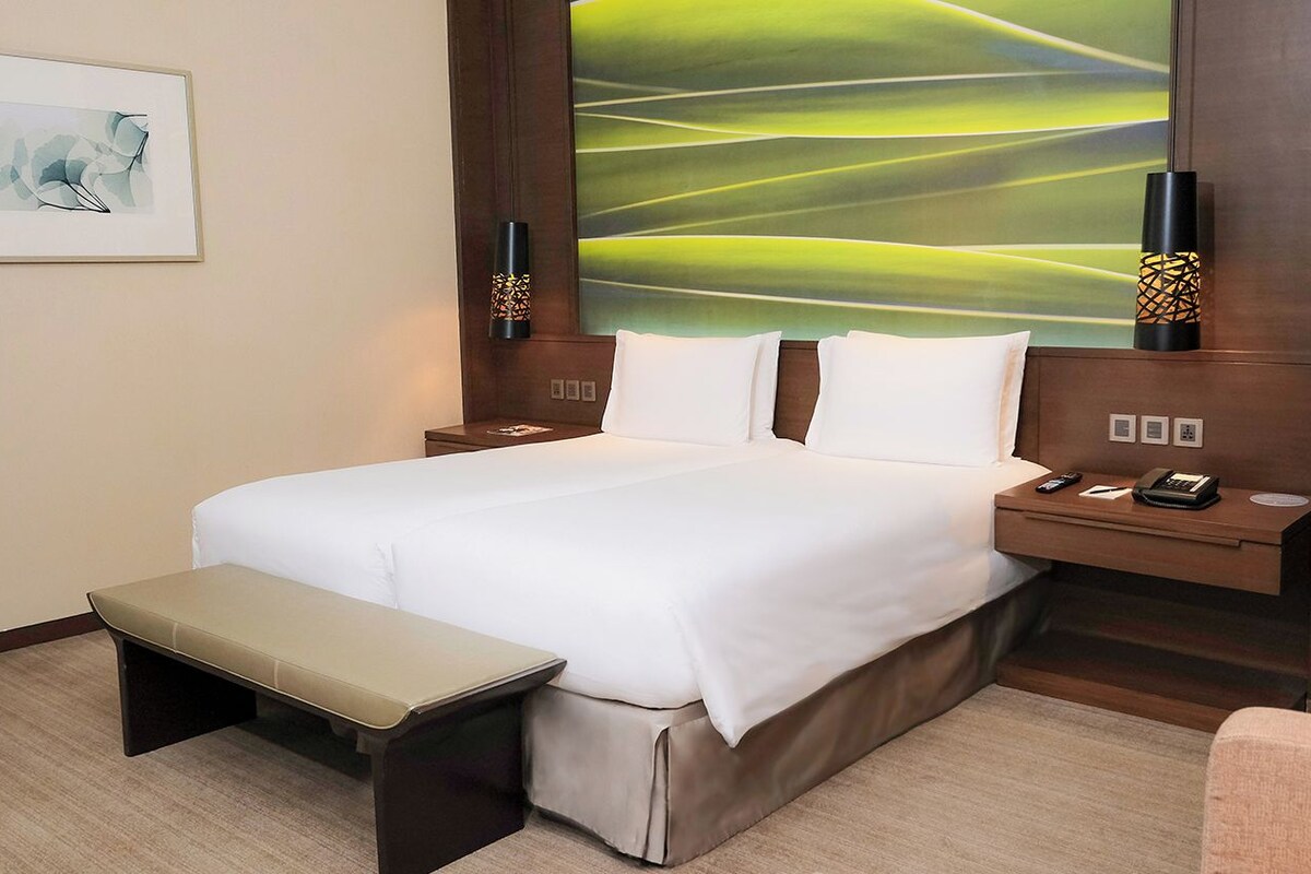 Una habitación de hotel con una cama, mesitas de noche, un banco y un cuadro abstracto grande en la pared.
