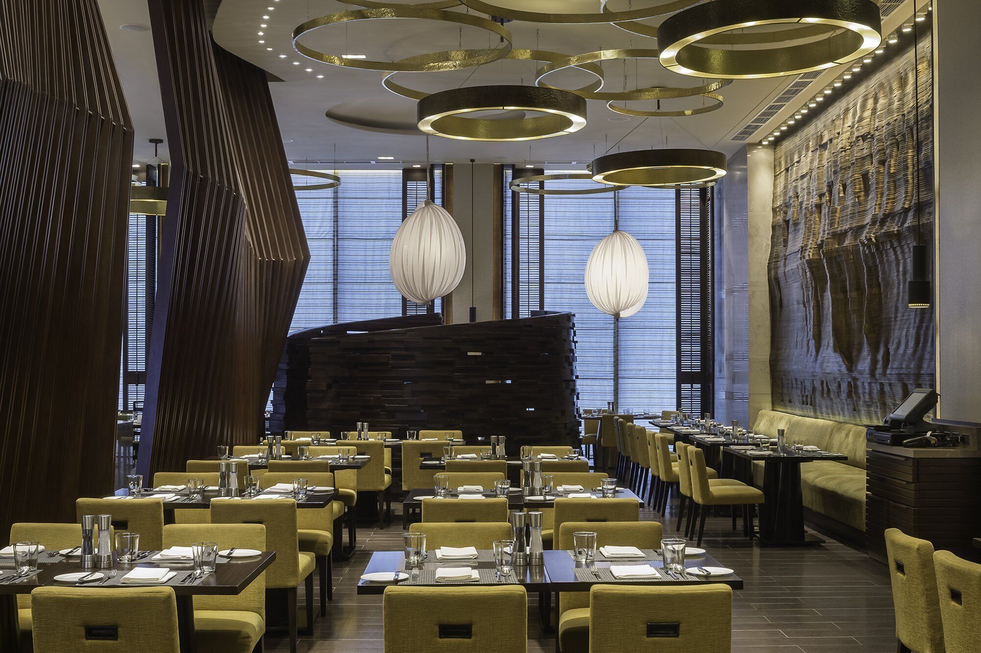 A modern restaurant with a central black structure, multiple dining tables, and unique lighting fixtures.