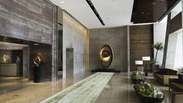 Un hall d’entrée moderne avec un comptoir de réception en marbre, une grande sculpture abstraite et un espace détente agrémenté de plantes.