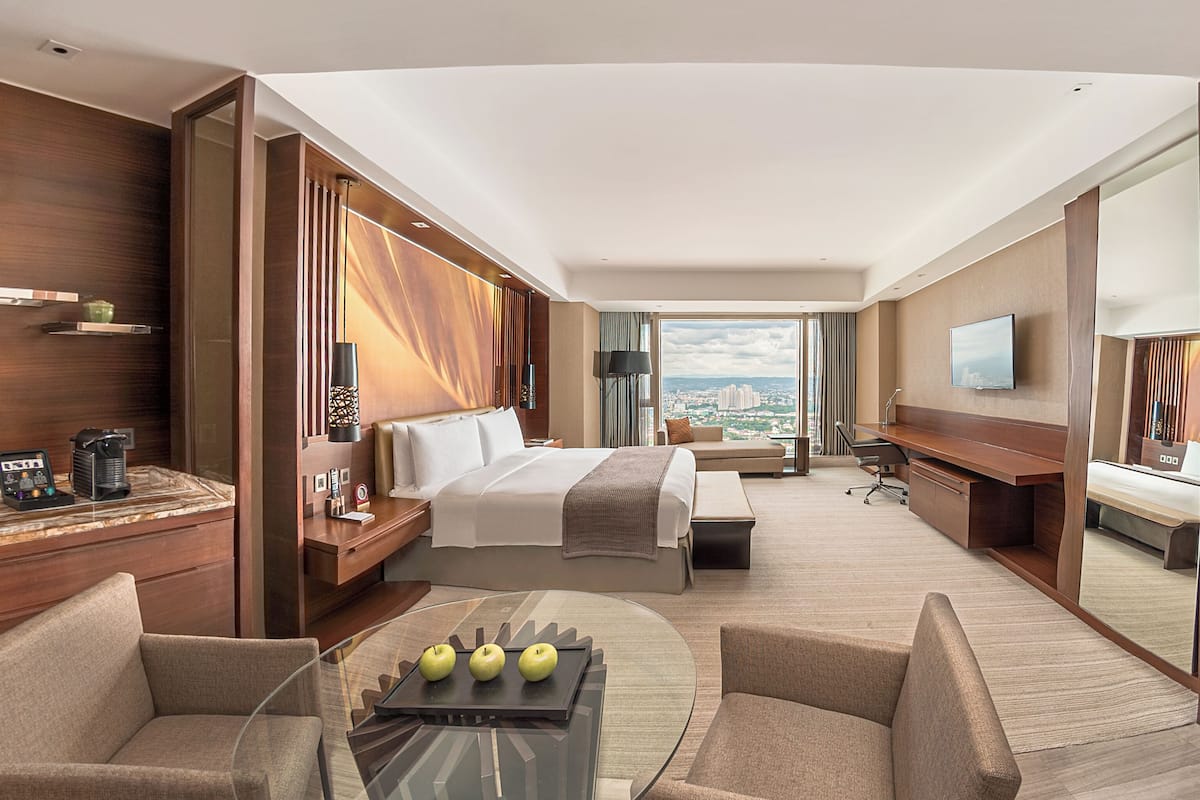 A modern hotel room with a large bed, a desk, a sofa, and a view of the city.