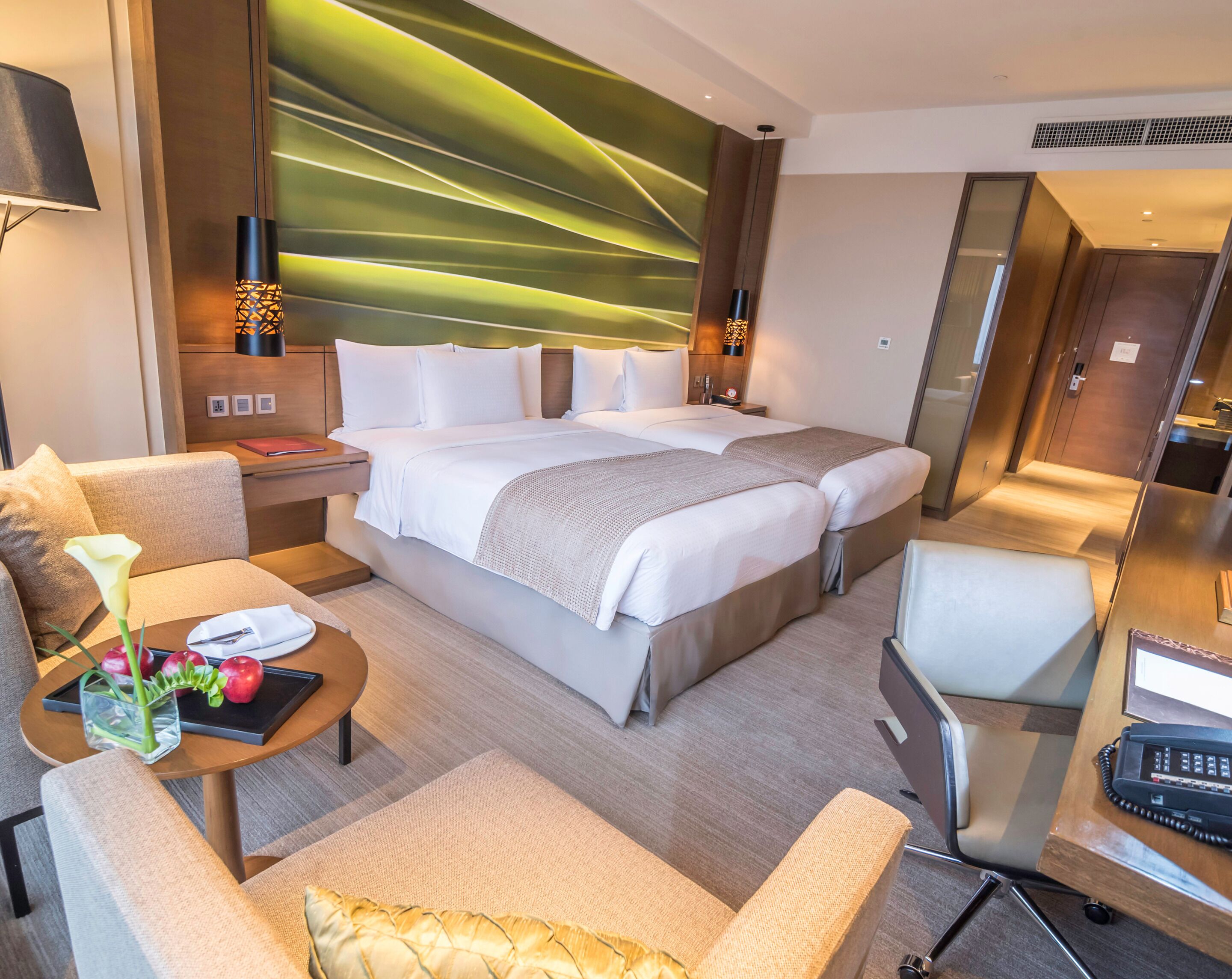 Ein modernes Hotelzimmer mit einem großen Bett, einem Schreibtisch, einem Stuhl und einem Nachttisch mit Lampe und Blumen.'