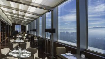 Un restaurante moderno con techos altos, ventanas amplias y vistas a la ciudad.