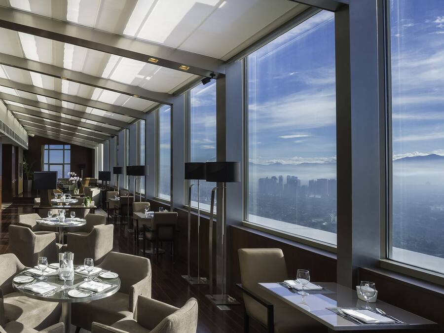 Un restaurante moderno con techos altos, ventanas amplias y vistas a la ciudad.