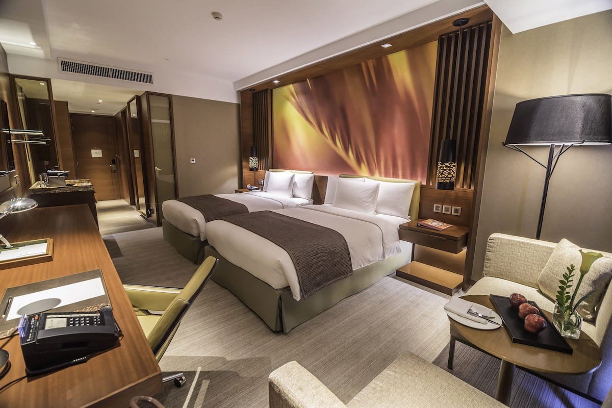 A modern hotel room with a large bed, a desk with a telephone, a chair, and a small table with decorative items.