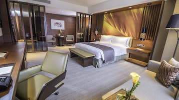 A hotel room with a bed, a desk, a chair, a sofa, and a bedside table with a vase of flowers.