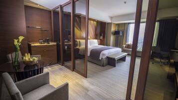 Una habitación de hotel moderna con una cama grande, un escritorio, una silla y un área de comedor con una mesa y sillas de vidrio.