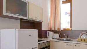 A compact kitchen with a refrigerator, oven, microwave, and a window with curtains. - Aparthotel Lighthouse (Sveti Vlas)