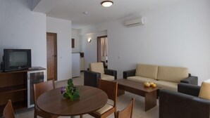 A modern living room with a round dining table, two sofas, a TV, and a small refrigerator. - Aparthotel Lighthouse (Sveti Vlas)