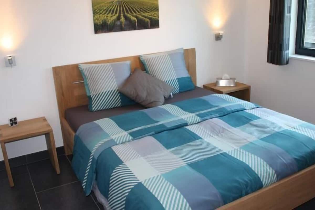 Ein Schlafzimmer mit einem hölzernen Bett, einer blau-weißen Streifenauflage, zwei Nachttischen und einer Wandleuchte.