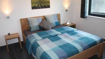 Een slaapkamer met een houten bed, een blauw-witte strepenbedekking, twee nachtkastjes en een wandlamp.