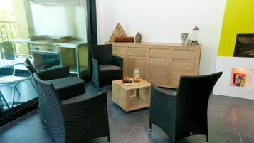 A modern living room with wicker furniture, a small wooden table with snacks, and a kitchen area visible through a glass door.