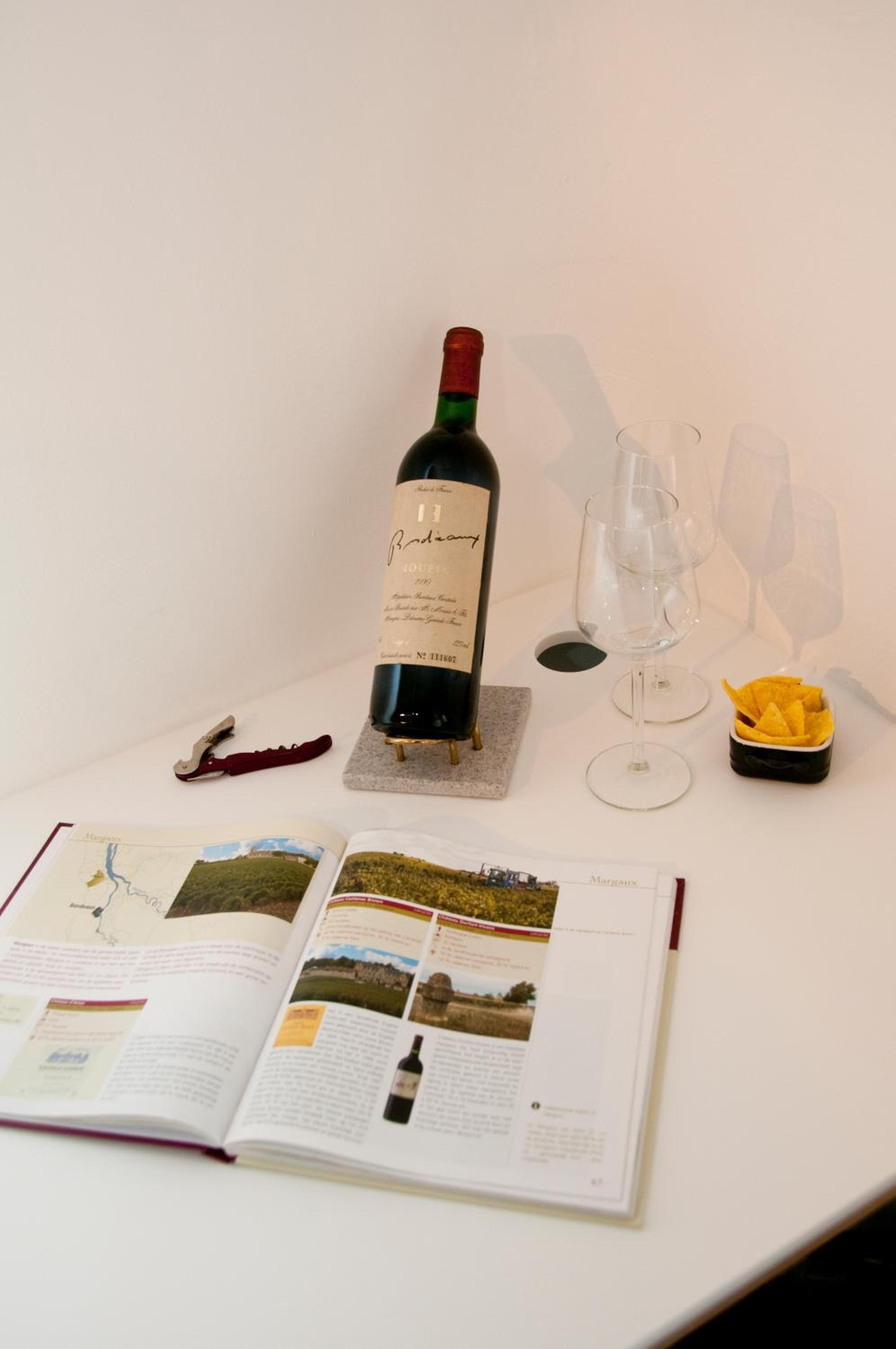 A wine bottle on a table with glasses and a book.