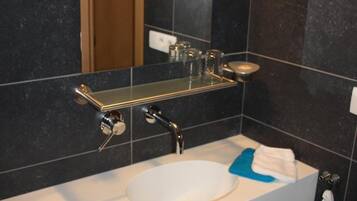 Un baño moderno con un lavamanos blanco, baldosas oscuras, un espejo y un perchero para toallas.