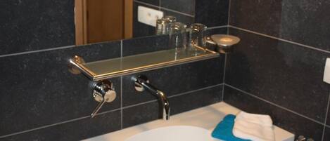 Un baño moderno con un lavamanos blanco, baldosas oscuras, un espejo y un perchero para toallas.