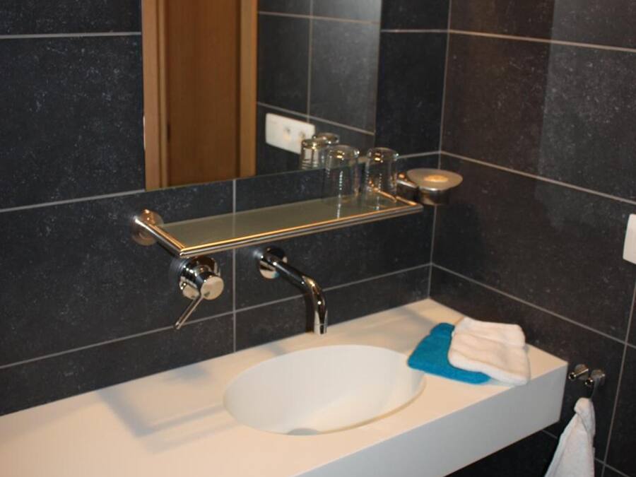 Un baño moderno con un lavamanos blanco, baldosas oscuras, un espejo y un perchero para toallas.