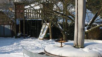 Un espacio exterior cubierto de nieve con un banco de metal y una estructura de juegos al fondo.