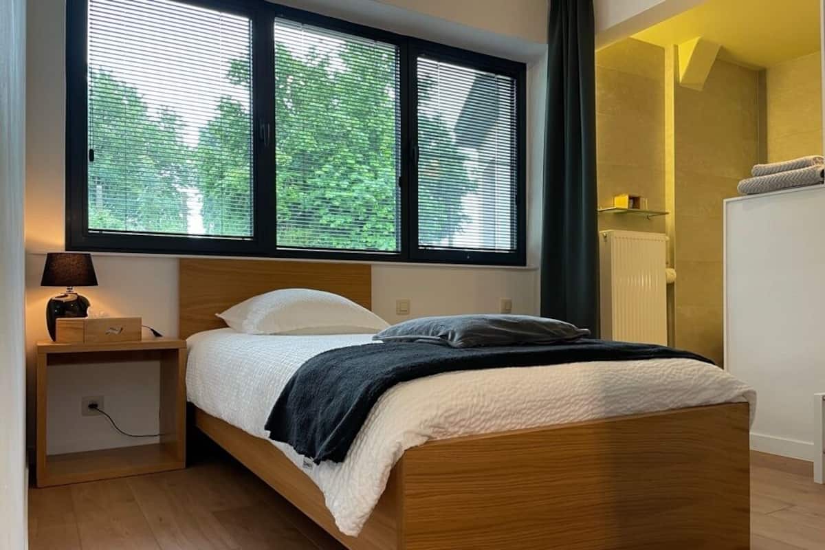 Ein Schlafzimmer mit einem hölzernen Bett, einem Nachttisch mit Lampe und einem Fenster mit Jalousien.