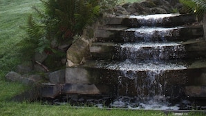 A house with a balcony, a small waterfall feature, and a well-maintained lawn. - Gasthof Kapelhof (Erpe-Mere)