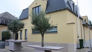 Ein Gebäude mit gelber Fassade, grauem Dach und einem kleinen Baum im Vordergrund.
