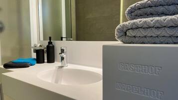 Un baño con un lavamanos blanco, un espejo y una pila de toallas.