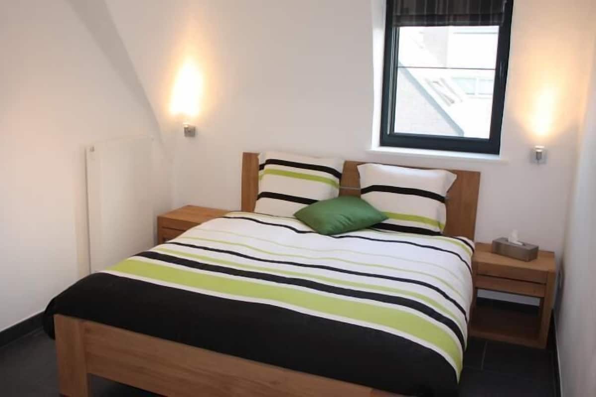 Ein Schlafzimmer mit einem Bett, zwei Nachttischen, einem Fenster und Wandleuchten.