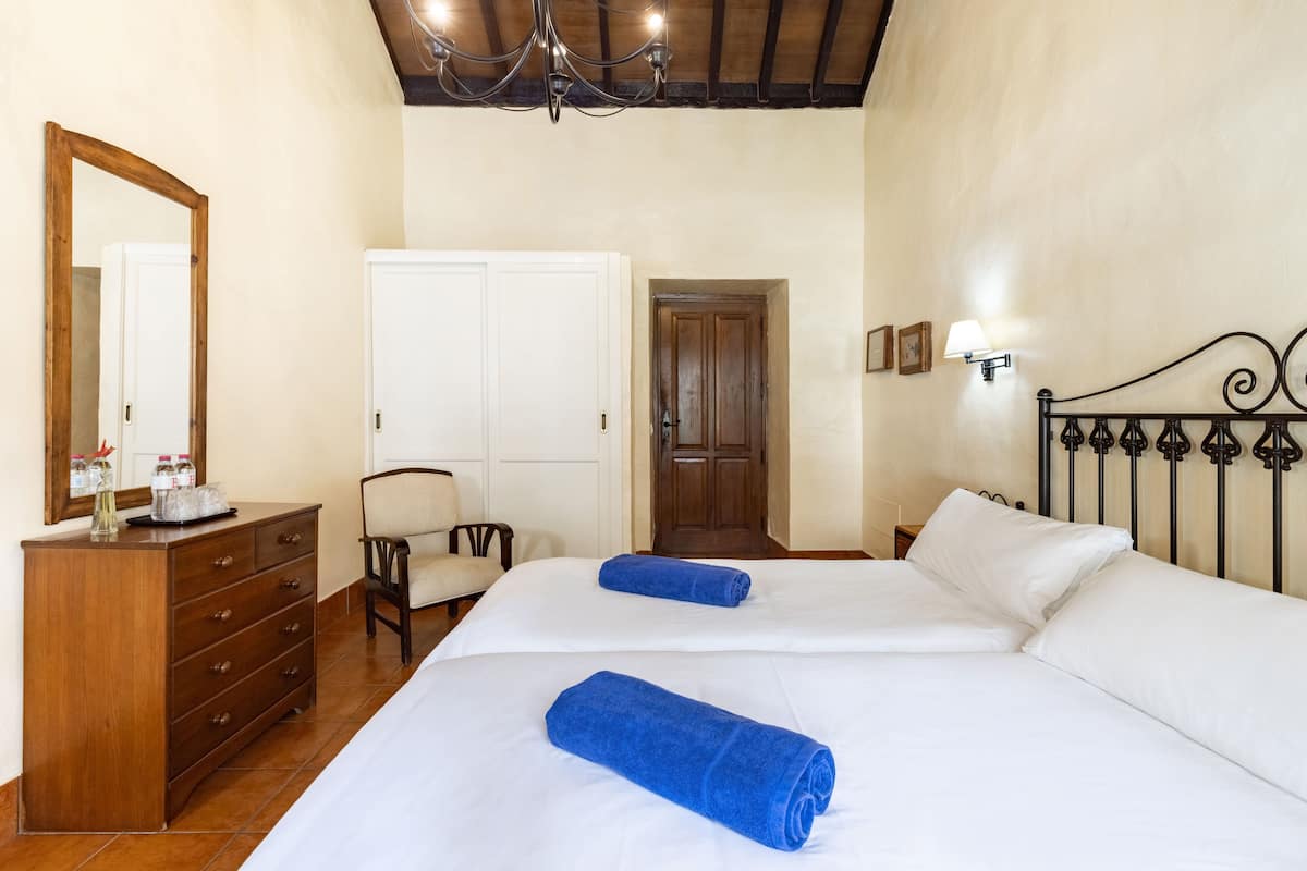 A bedroom with two beds, a wooden dresser, a chair, a wardrobe, a chandelier, and a door.