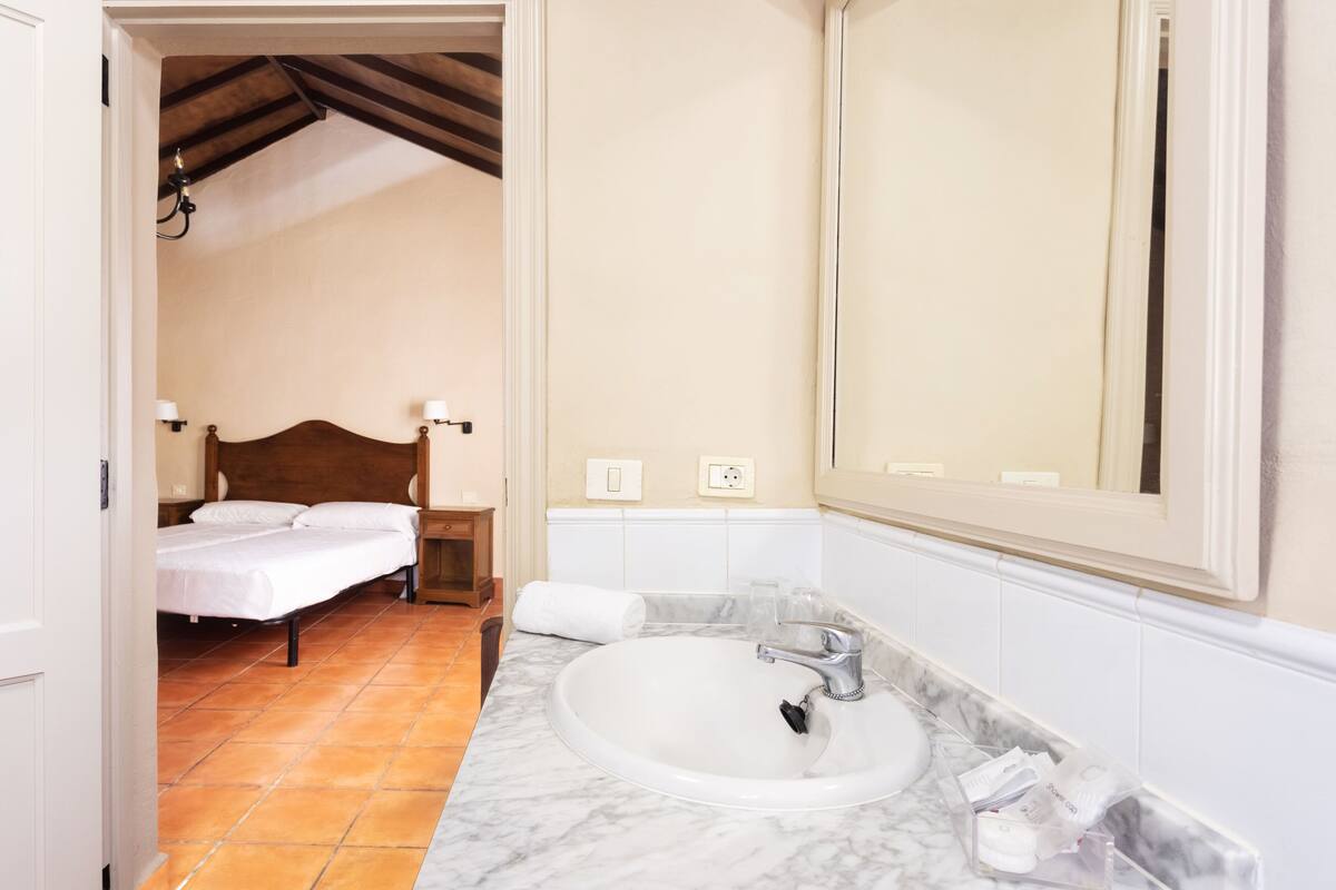 A bedroom with a bed, a nightstand, a bathroom with a sink and mirror.
