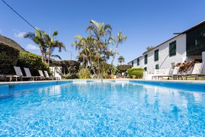 A clear blue pool surrounded by white buildings with green shutters, palm trees, and lounge chairs. - Hotel El Patio (Garachico)