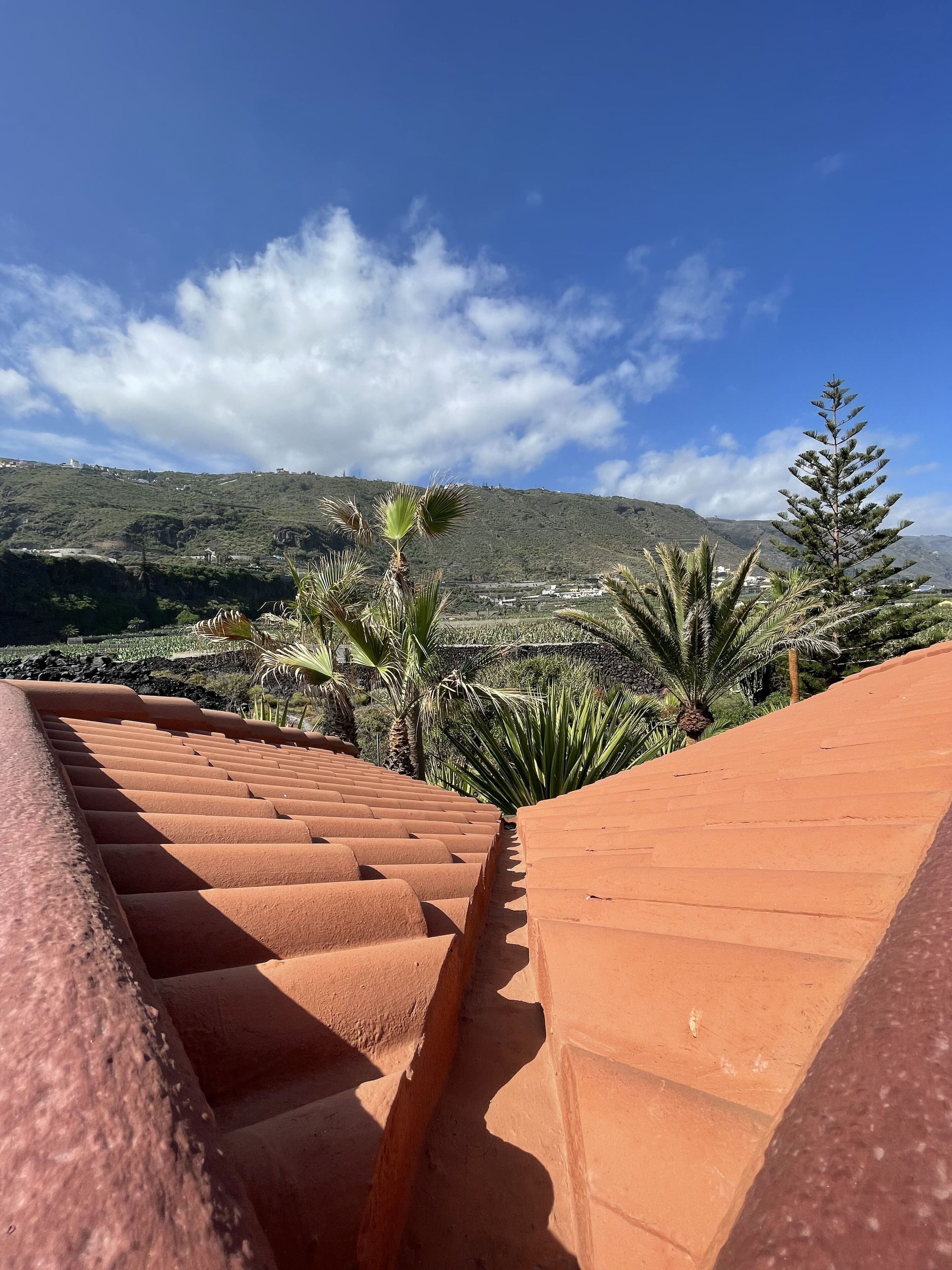 Eine mit Terrakotta-Fliesen ausgelegte Treppe führt zu einer Terrasse mit Blick auf eine Hügelkuppe und Gebäude in der Ferne.