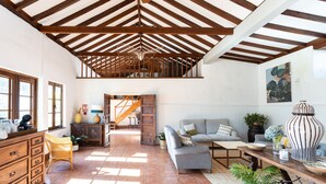 Un salón amplio con techos altos, vigas de madera, una escalera, un sofá, una mesa de centro y una mesa de comedor.