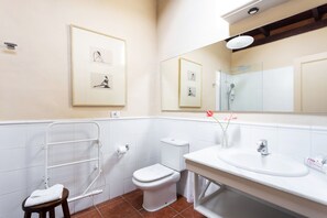 Un baño con inodoro, lavamanos y ducha. Hay cuadros enmarcados en la pared y una toalla en el suelo.